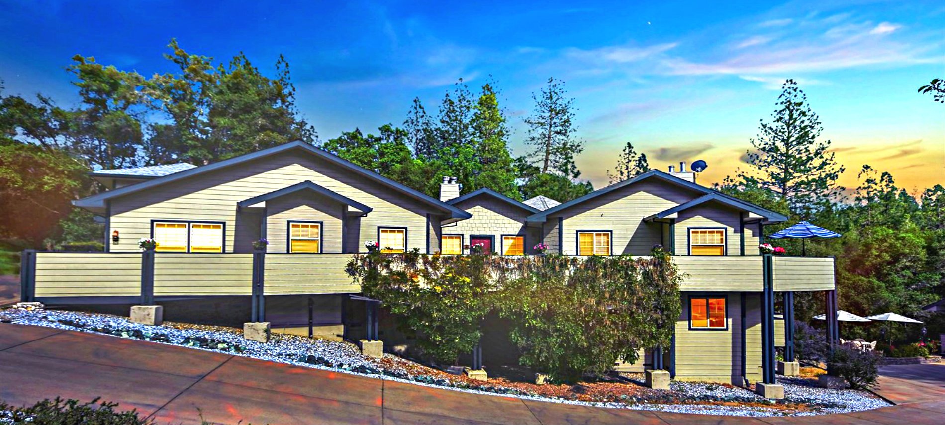 The Inn with blue sofits and beige horizontal siding sitting amongst green trees and shrubs. 